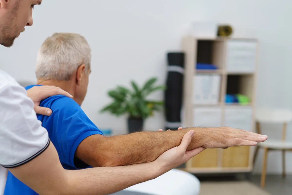 Physiotherapist giving hands-on shoulder and arm treatment to an older man during a home visit