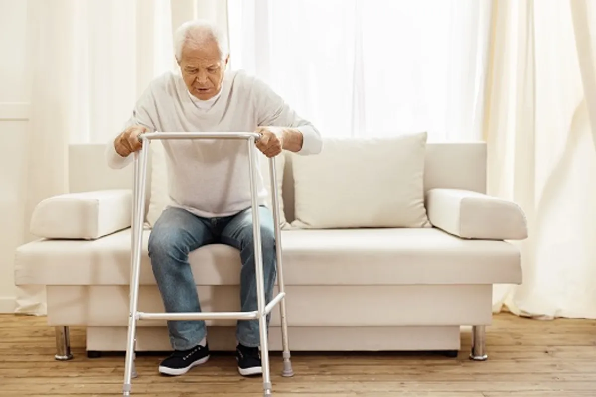 Older man practising standing up safely with a walking frame during a home physiotherapy visit
